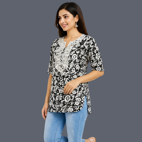 A woman wearing a black and white floral print kurta with white embroidery on the chest, paired with light blue jeans, against a plain light gray background.