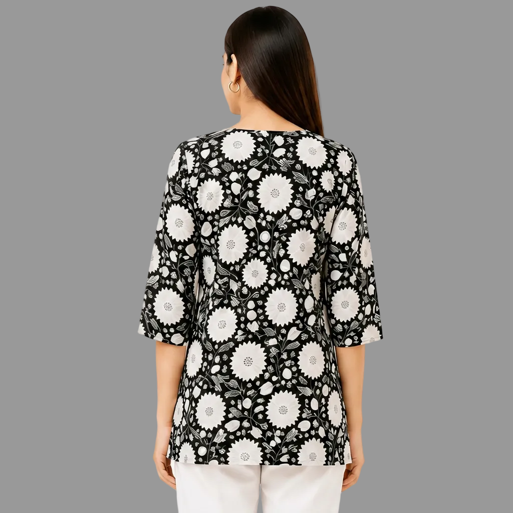 A woman viewed from the back wearing a black three-quarter sleeve top with a white floral pattern, paired with white pants, against a white background.