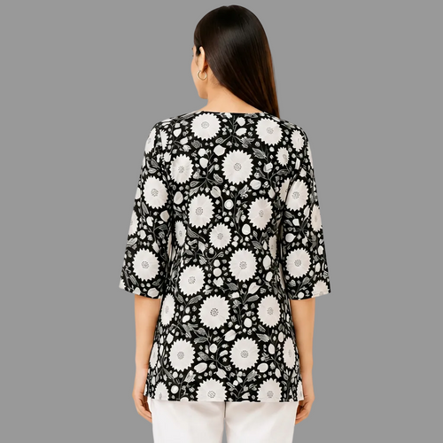 A woman viewed from the back wearing a black three-quarter sleeve top with a white floral pattern, paired with white pants, against a white background.