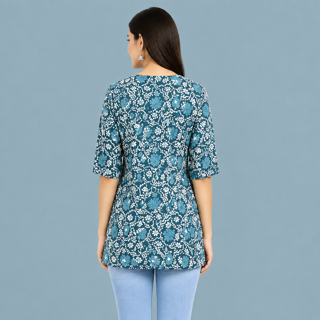 A woman shown from the back wearing a teal blue and white floral print tunic top with three-quarter sleeves, paired with light blue jeans, against a white background.