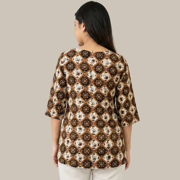 A woman viewed from the back wearing a brown, beige, and white patterned top with three-quarter sleeves and white pants, set against a plain white background.