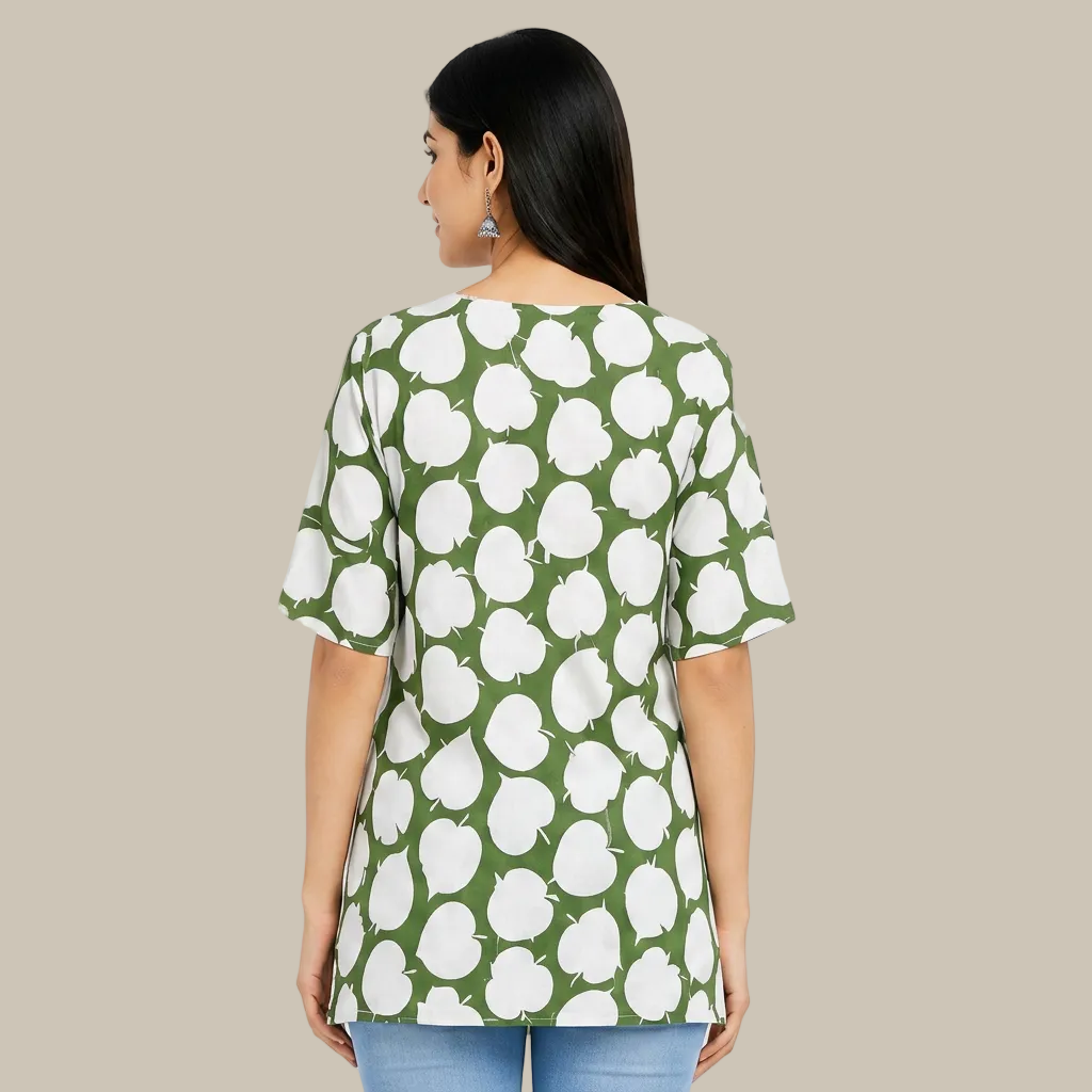 A woman shown from the back wearing a loose short-sleeve top with a green and white apple print, paired with light blue jeans, against a plain white background.