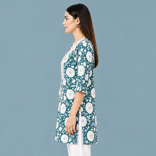 A woman shown in side profile wearing a teal and white floral print tunic top with three-quarter sleeves and a cream inner layer, photographed against a plain white studio background.