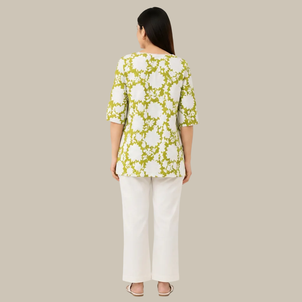 A woman viewed from the back wearing a green and white floral print top with three-quarter sleeves and white pants, set against a plain white background.