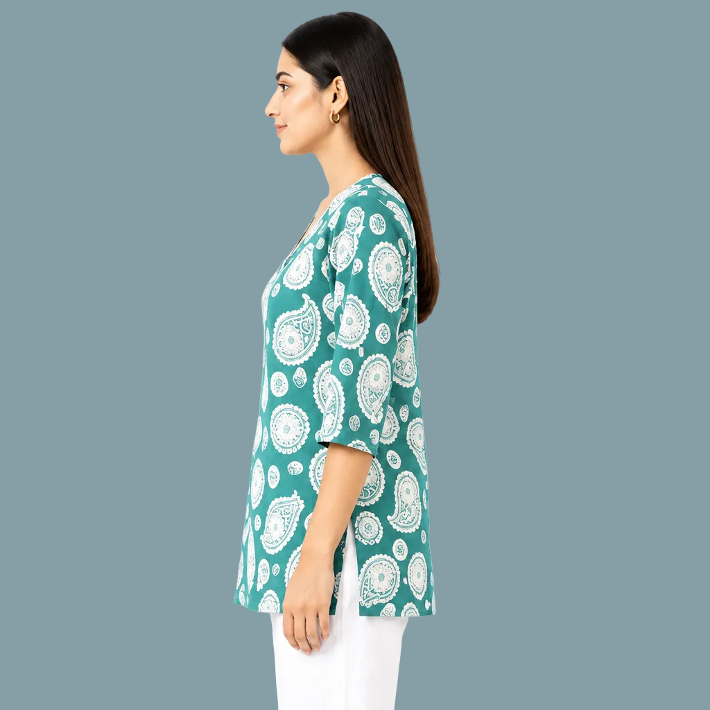 A woman shown in side profile wearing a teal green tunic top with a white paisley pattern, paired with white pants, against a plain white background.