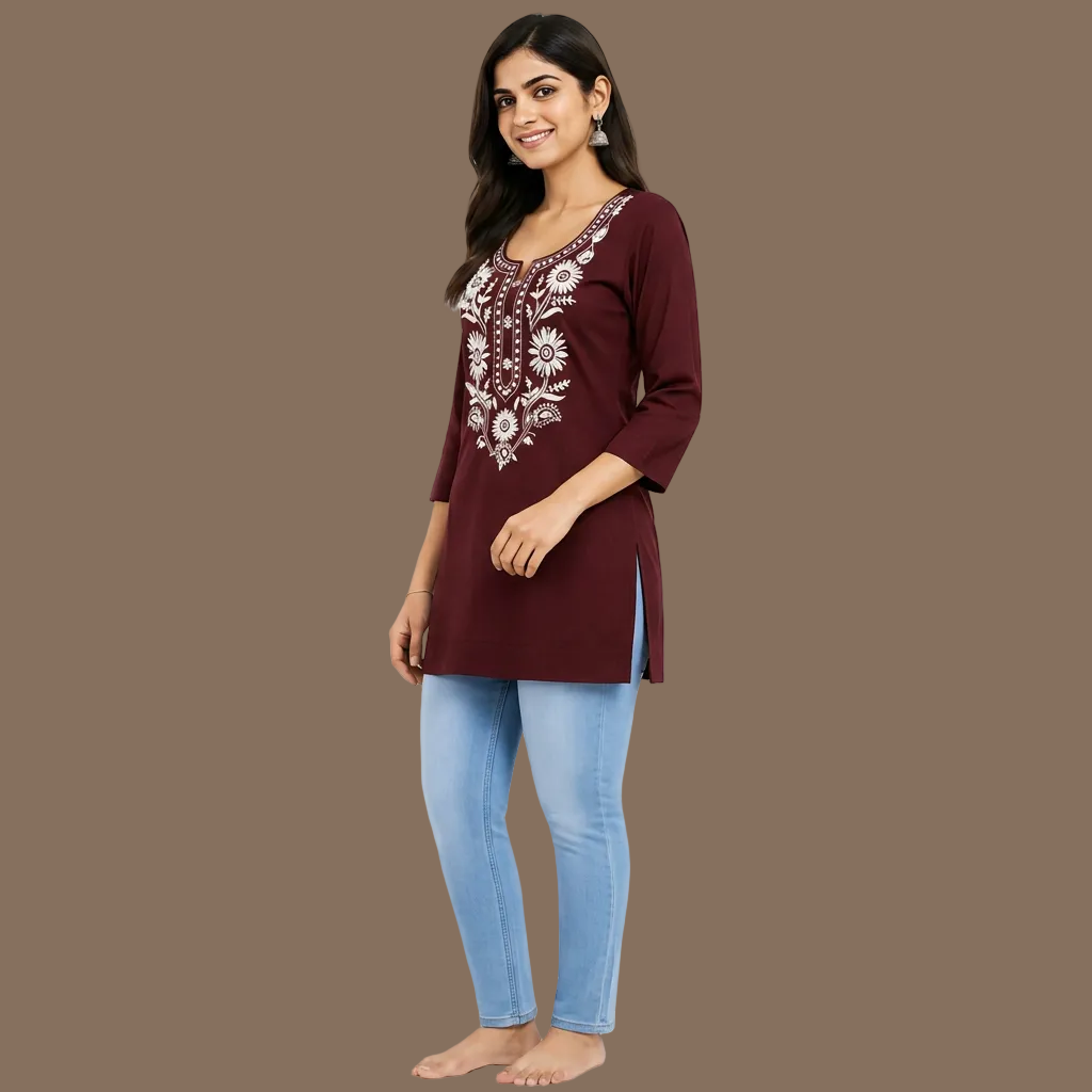 A woman wearing a maroon three-quarter sleeve kurta with white floral embroidery on the chest, paired with light blue jeans, set against a plain light gray background.