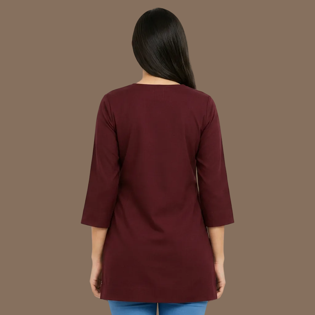 A woman shown from the back wearing a three-quarter sleeve tunic top in a deep burgundy color, paired with light blue jeans, against a plain light gray background.