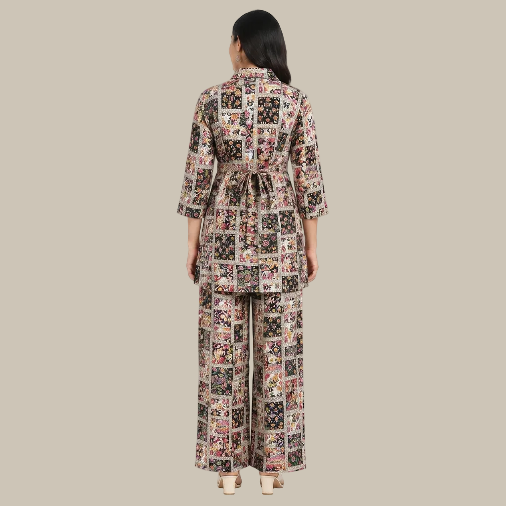 A woman shown from the back wearing a matching two-piece set consisting of a long-sleeve belted jacket and wide-leg pants, both covered in a colorful patchwork floral print. She is standing against a plain white background.