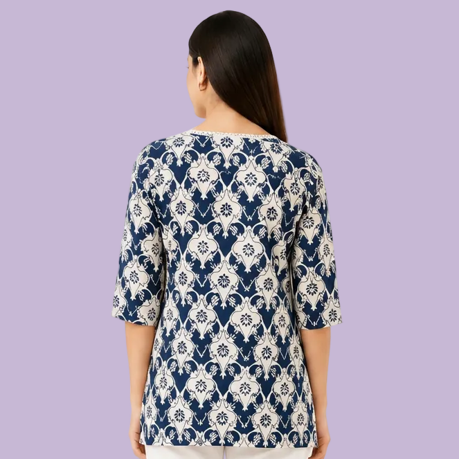 A woman shown from the back wearing a navy blue and white damask-patterned top with three-quarter sleeves, paired with white pants, against a plain white background.