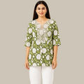 A woman modeling a green and white floral print tunic top with white lace detailing on the chest and sleeves, set against a plain white background.