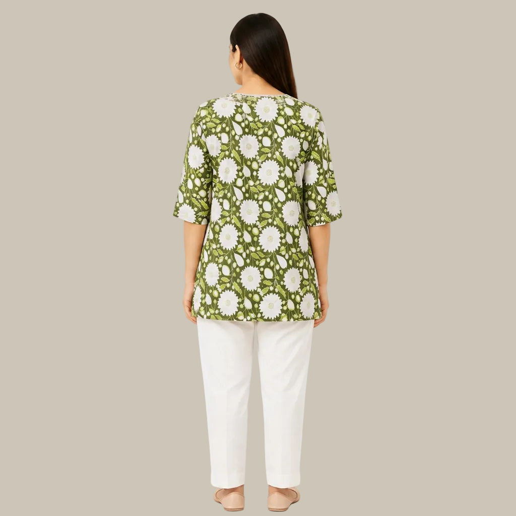 A woman viewed from the back wearing a green short-sleeve top with a white daisy floral pattern, paired with white pants, against a plain white background.