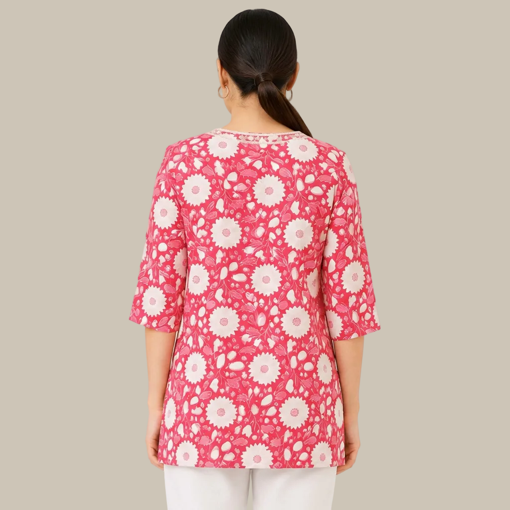 A woman viewed from the back wearing a pink three-quarter sleeve top with a white floral pattern, paired with white pants, against a plain white background.