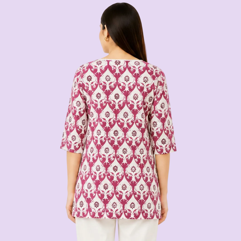 A woman viewed from the back wearing a pink and white patterned tunic top with three-quarter sleeves and white pants, set against a plain white background.