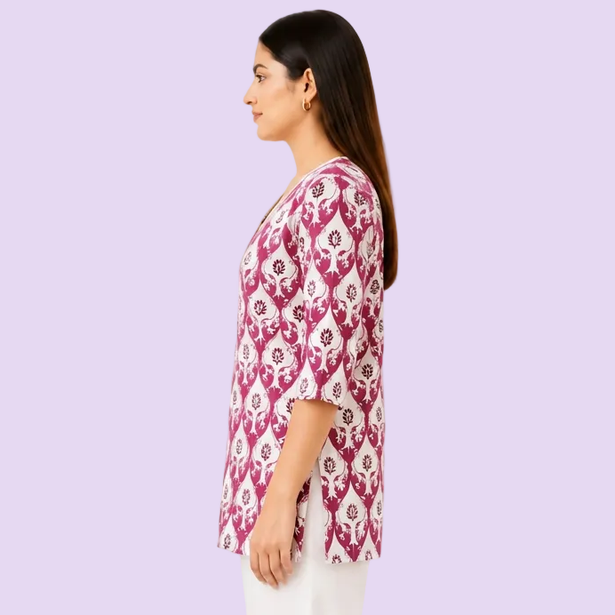 A woman shown in side profile wearing a short-sleeve V-neck tunic top with a magenta and white floral block print pattern, paired with white pants, against a plain white background.
