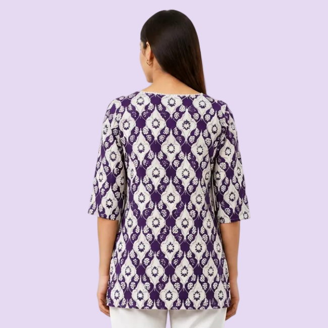 A woman viewed from the back wearing a purple and white patterned tunic top with three-quarter sleeves and white pants, set against a plain white background.
