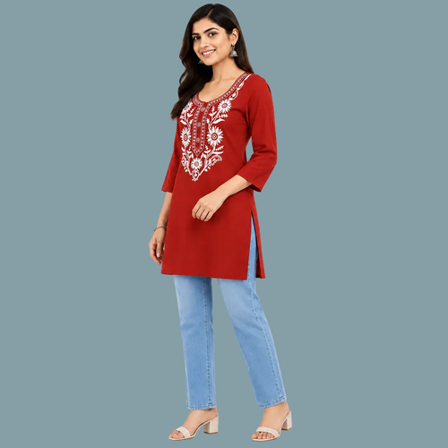 A woman wearing a red three-quarter sleeve kurta with white floral embroidery on the chest, paired with light blue jeans, set against a plain light gray background.